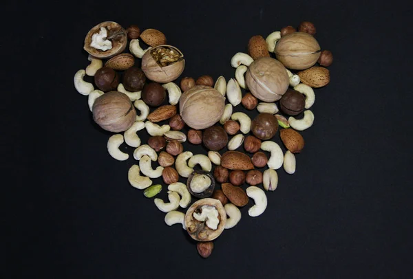 Heart symbol made of nuts. Nuts on dark background. Assorted mixed nuts  on black background.