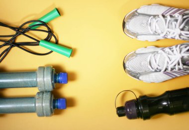 Sarı arka planda spor envanterli kompozisyon. Spor konsepti düzleşir. Sağlık için spor ayakkabıları ve su için şişe. Uzayı kopyala, afiş.