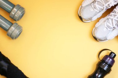 Sarı arka planda spor envanterli kompozisyon. Spor konsepti düzleşir. Sağlık için spor ayakkabıları ve su için şişe. Uzayı kopyala, afiş.