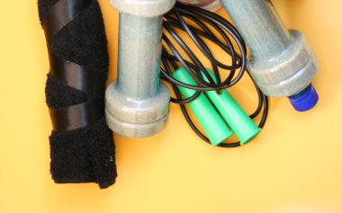 Halat, su şişesi, dambıl ve spor ayakkabıları sarı arka planda. Fitness, spor ve sağlıklı yaşam tarzı kavramı.