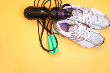 Halat, su şişesi, dambıl ve spor ayakkabıları sarı arka planda. Fitness, spor ve sağlıklı yaşam tarzı kavramı.