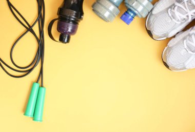 Sarı arka planda spor envanterli kompozisyon. Spor konsepti düzleşir. Sağlık için spor ayakkabıları ve su için şişe. Uzayı kopyala, afiş.