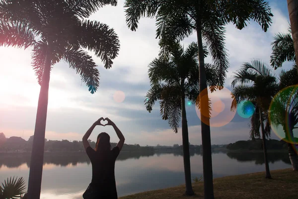 Silueta de mujer joven haciendo un corazón en forma de mano al amanecer — Foto de Stock