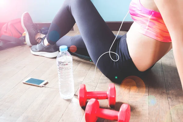 Fitness-Frau in schwarzer Hose und Turnschuhen entspannt nach dem Training mit Kurzhanteln und Wasserflasche — Stockfoto