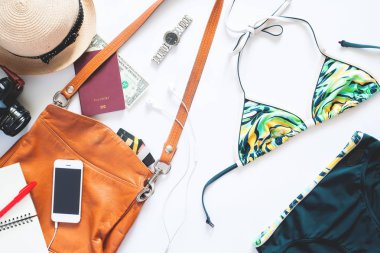 Düz yaz öğeleri kümesi yatıyordu. Kız öğelerle bikini, izle, cep telefonu, fotoğraf makinesi ve pasaport beyaz zemin üzerine yaz tatili için