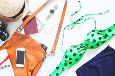 Düz yaz öğeleri kümesi yatıyordu. Kız öğelerle bikini, izle, cep telefonu, fotoğraf makinesi ve pasaport beyaz zemin üzerine yaz tatili için