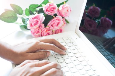 Pembe gül buketi ile dizüstü bilgisayar kullanan kadın. Alışveriş 