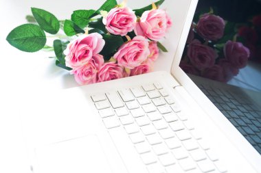 Dizüstü bilgisayar ile arka planda pembe gül buketi. Teknoloji