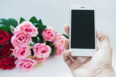 Kadın el cep telefonu gül buket arka plan ile tutarak