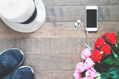 Kırmızı ve pembe güller, şapka ve kopya alanı ile ahşap zemin üzerinde spor ayakkabı ile Smartphone