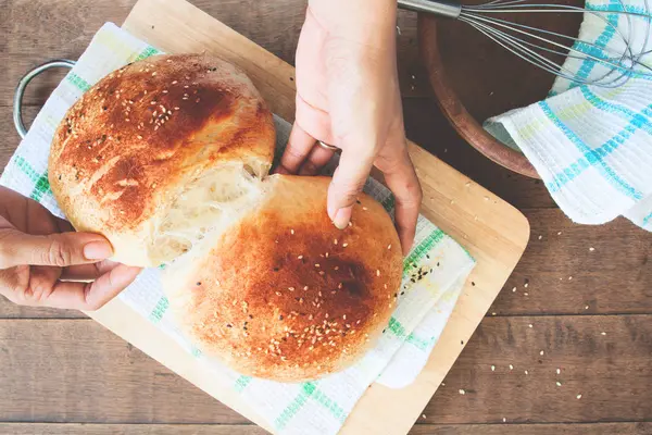 Mulher mão segurando pão caseiro com gergelim no fundo da mesa de madeira — Fotografia de Stock