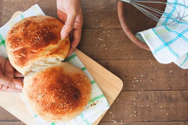 Frau hält Laib hausgemachtes Brot mit Sesam auf Holztischhintergrund — Stockfoto