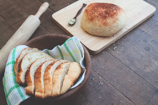 Булочка и нарезанный домашний хлеб с кунжутом и кухонными инструментами на деревянном фоне с копировальным пространством — стоковое фото