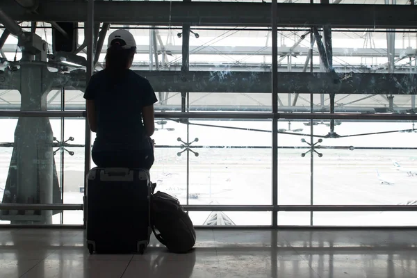 Γυναίκα ταξιδιώτης κάθεται στο αποσκευών βαλίτσα στο αεροδρόμιο, σιλουέτα με θέα στο αεροδρόμιο — Φωτογραφία Αρχείου