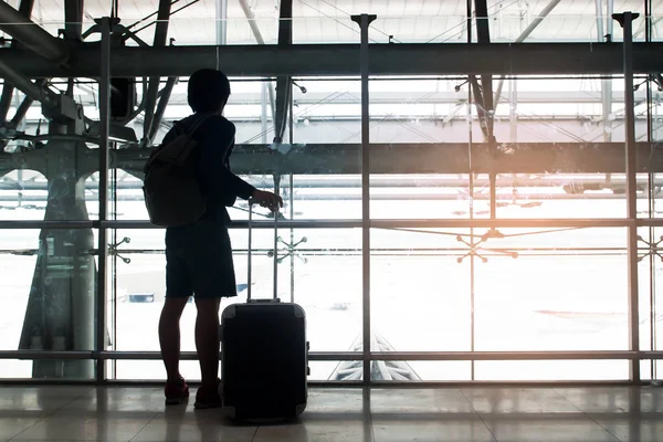 Σιλουέτα του ταξιδιώτη με αποσκευών βαλίτσα και σακίδιο ματιά έξω από το παράθυρο στο αεροδρόμιο — Φωτογραφία Αρχείου