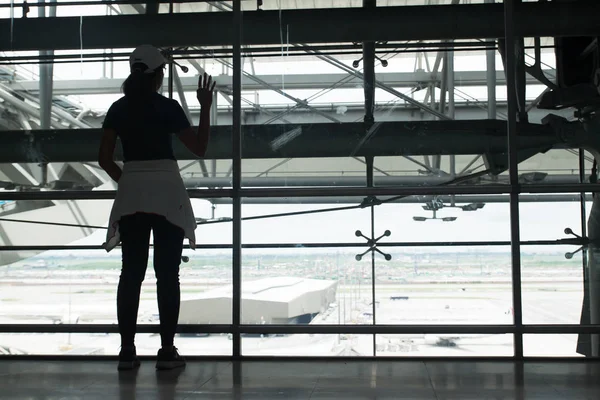 Silhouette of a young woman look out of the window at airport say good bye to her family