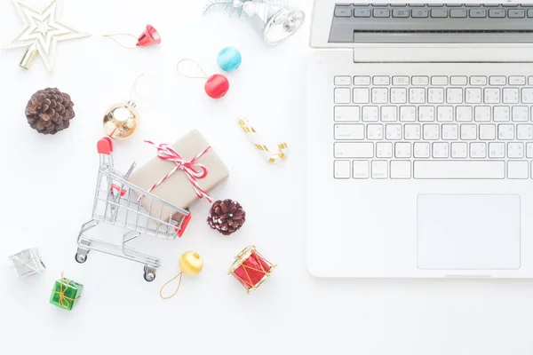 Vánoční dekorace a dárkové krabičky v nákupním košíku a notebook, on-line nákupní koncept pohled shora — Stock fotografie