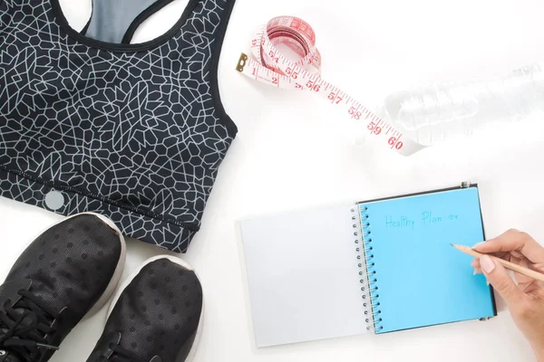 Yaratıcı düz sağlıklı kavramı, defter ve fitness öğeler beyaz arka plan üzerinde kalem tutan kadın yatıyordu.