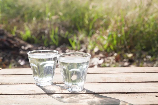 Bicchieri di acqua pura sul tavolo di legno con la natura in background, stile di vita sano — Foto Stock