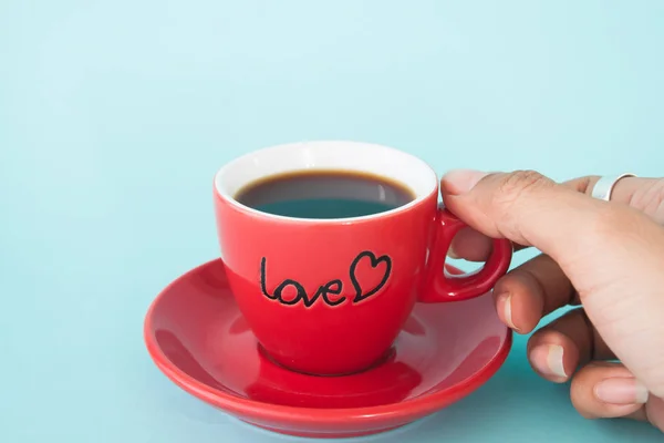 Kvinnas hand hålla röd kopp kaffe med kärlek på pastell färg, kärlek och alla hjärtans dag koncept — Stockfoto