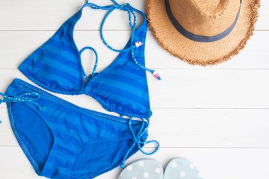 Bikini, hasır şapka ve sandalet Beyaz ahşap zemin, üstten görünüm üzerinde seyahat ve tatil kavramı