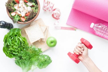 Beyaz arka planda, sağlıklı kavramı salata kasesi, sebze, elma ve dilimlenmiş ekmek, fitness aletleri ve kadının el holding dumbbell Üstten Görünüm