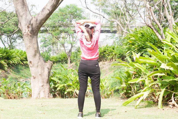 Pohled zezadu na sportovní žena v růžové košili, táhnoucí se před tréninkem v parku, zdravého životního stylu — Stock fotografie