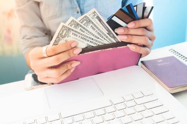 Kadının elleri cüzdan gösteren dolar faturaları ve kredi kartları dizüstü bilgisayar ve pasaport kitap çalışma masası, iş ve finans, seyahat kavramı üzerinde açık 
