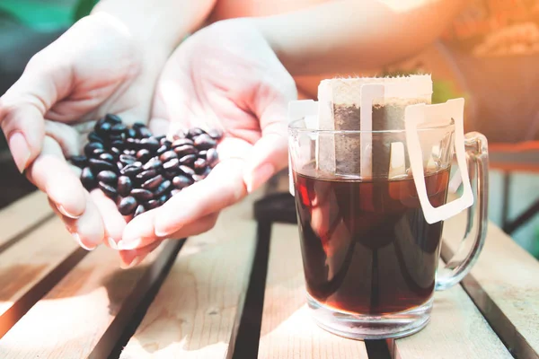 Saco de gotejamento café fresco em vidro com as mãos da mulher segurando grãos de café — Fotografia de Stock
