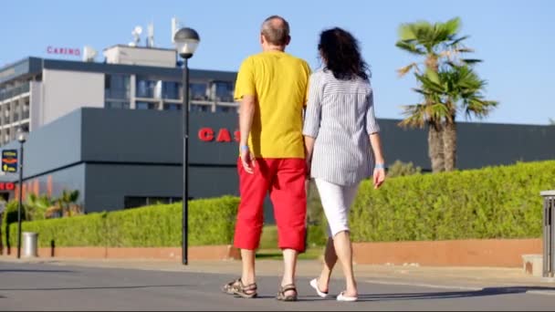 Volwassen paar op vakantie, ze lopen over de strandboulevard hand in hand. — Stockvideo