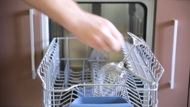 Man is putting a few wine glasses and tea caps into a dishwasher. — Stock Video