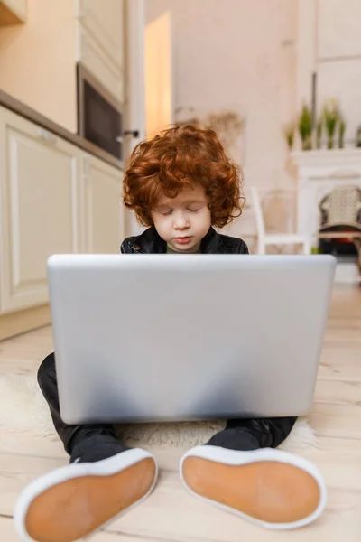 Piccolo ragazzo rossa utilizza un computer portatile — Foto Stock