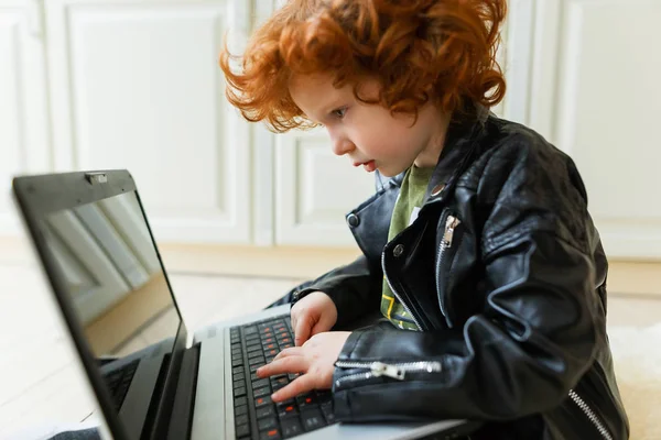 Piccolo ragazzo rossa utilizza un computer portatile — Foto Stock