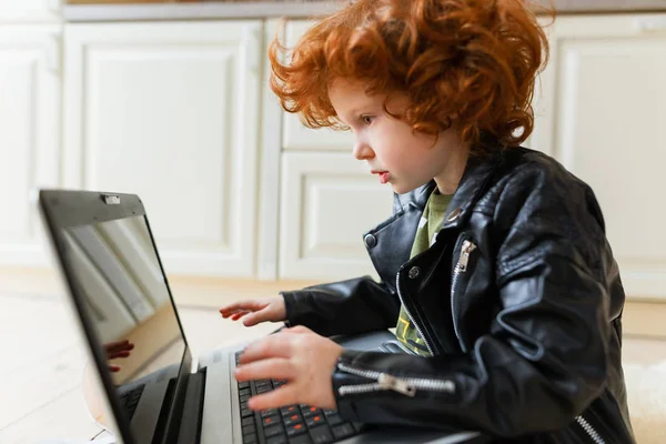 Pequeno menino ruivo usa um laptop — Fotografia de Stock