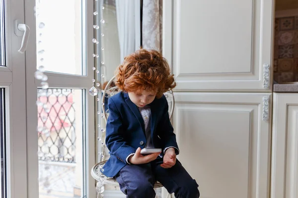 Little redhead boy uses a smartphone — Stock Photo, Image