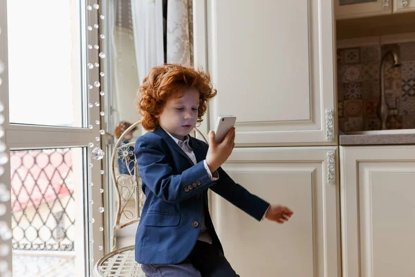 Маленький рудий хлопчик використовує смартфон — стокове фото