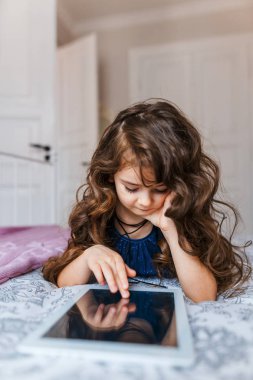 Dijital tablet kullanarak kıvırcık saçlı sevimli küçük kız 