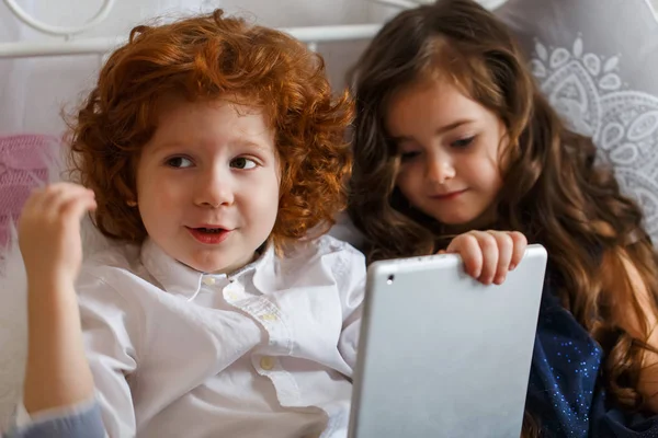 A boy and a girl lie on the bed and pla — Stock Photo, Image