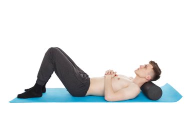Yakışıklı adam egzersiz yapıyor. Stüdyodaki spor minderinde miyofasyal masaj için köpük silindiri kullanıyor. Beyazda izole edilmiş.