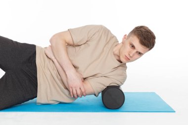 Yakışıklı adam, tetikleyici noktaların miyofasyal masajı için köpük silindiri kullanarak egzersiz yapıyor. Omuz kası masajı. Beyazda izole edilmiş.