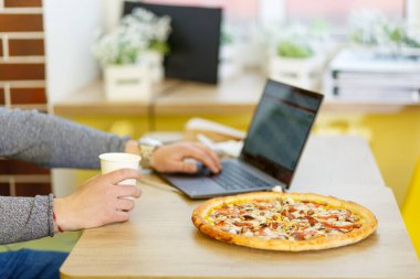 İş ya da öğrenim kavramı. Kafedeki bir masada pizza duruyor. Bir insan yemek yemeyi ve bilgisayarda çalışmayı birleştirir..