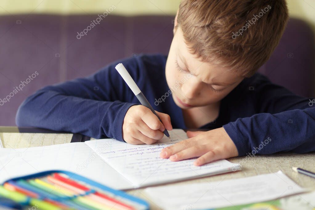 Schooler is engaged in home schooling. The boy sits at a table, writes, draws and learns online on the Internet. Quarantine due to the coronavirus pandemic, covid-19