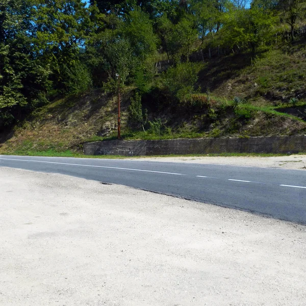 Local paved road. On one side is a hill with nature, and on the other side of the road is a surface with a breakstone