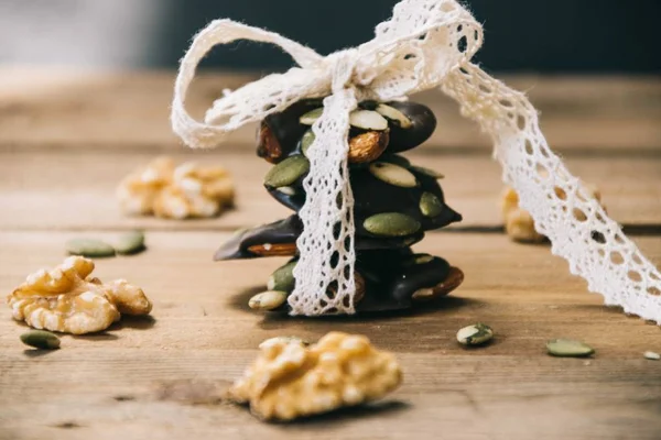 Close up of a pack of healthy snacks made from almonds, walnuts, hazelnuts and pumpkin seeds tied up with white lace on a wooden base — Stock Photo, Image