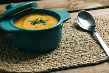 Saf sebzeli turkuaz tencere zeytinyağı ve hasırın üzerinde tahta bir kaşıkla soğan.