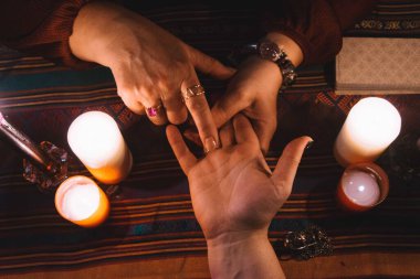 Parmaklarında mücevherler, mumlar ve masanın etrafında tarot destesiyle el okuyan bir kadın. Okültizm kavramı