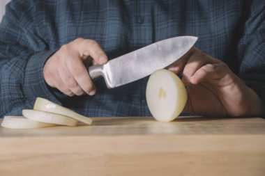 Keskin bir bıçakla kesen erkek elleri ahşap bir masada dilimlenmiş soğan. Yemek pişirme konsepti