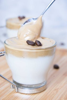 Bir kaşığın, bambu tepsisindeki bir bardak sütün üzerinde çiğ kahve çekirdekleri ile çırpılmış kahveyi kaptığı resmi yakından çek. Dalgona kahve konsepti