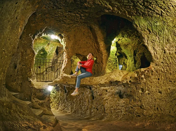 Mujer joven sentada en la roca. Derinkuyu cueva ciudad subterránea, Capadocia —  Fotos de Stock