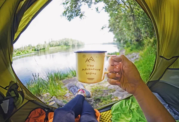 Молодая женщина сидит в палатке и пьет чай, глядя на реку Десна — стоковое фото